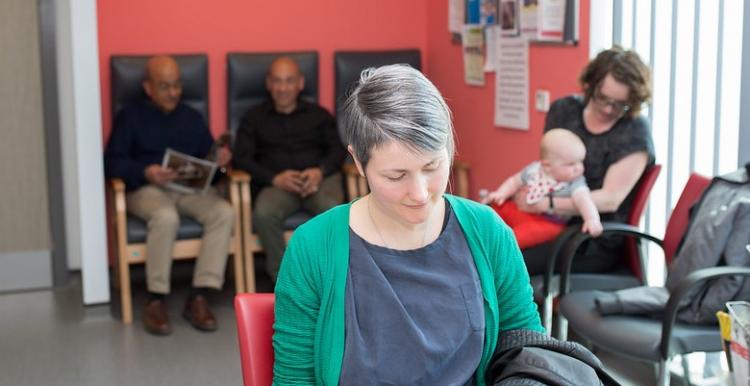 A lady sitting in a waiting room reading a magazine