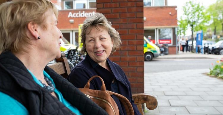 Two ladies sitting outside a hospital on a bench