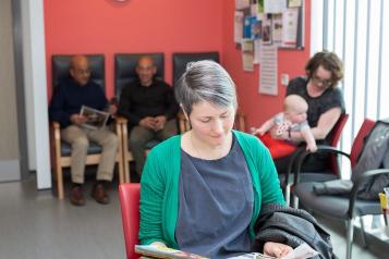 A lady sitting in a waiting room reading a magazine